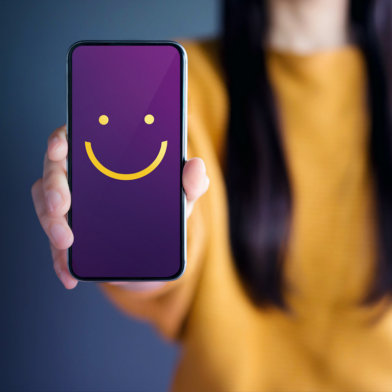 A woman holding a phone that shows a smile emoji, exceptional customer service