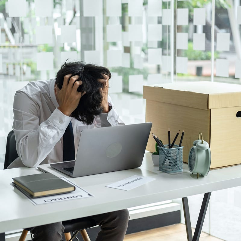 An employee holding his head between his hands on the table with a laptop.